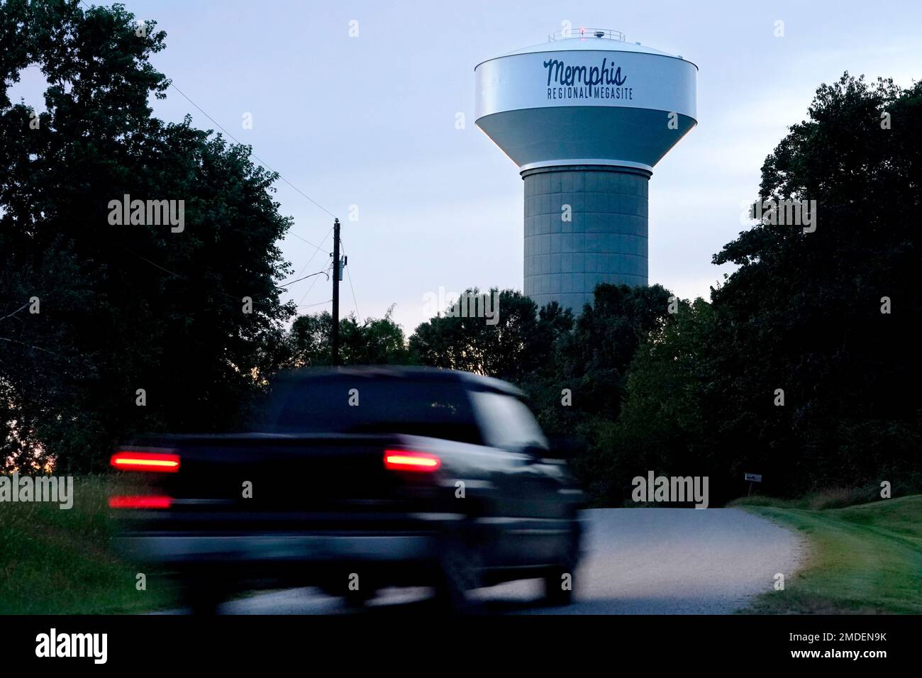 A truck drives down a rural road near a water tower marking the