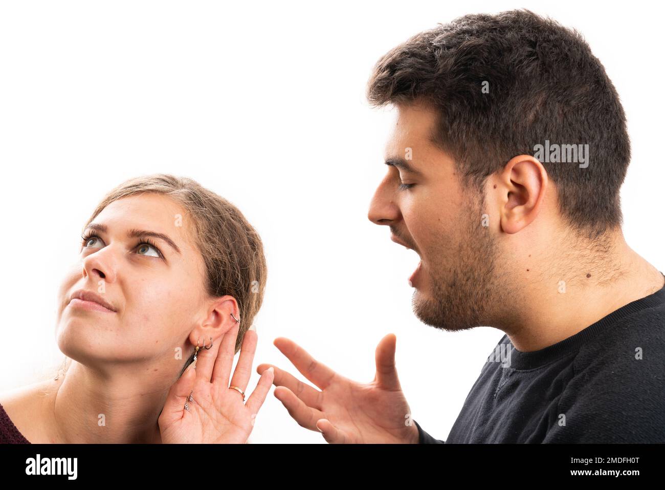 Adult girlfriend making listening gesture with hand to ear while boyfriend yelling talking as relationship communication concept isolated on white stu Stock Photo