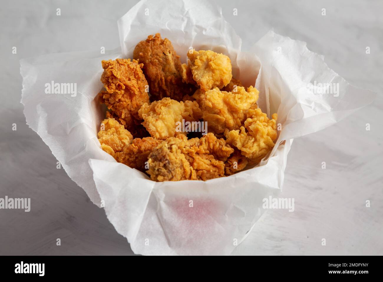 Chicken popcorn, wings, tenders in paper box on a gray background, side