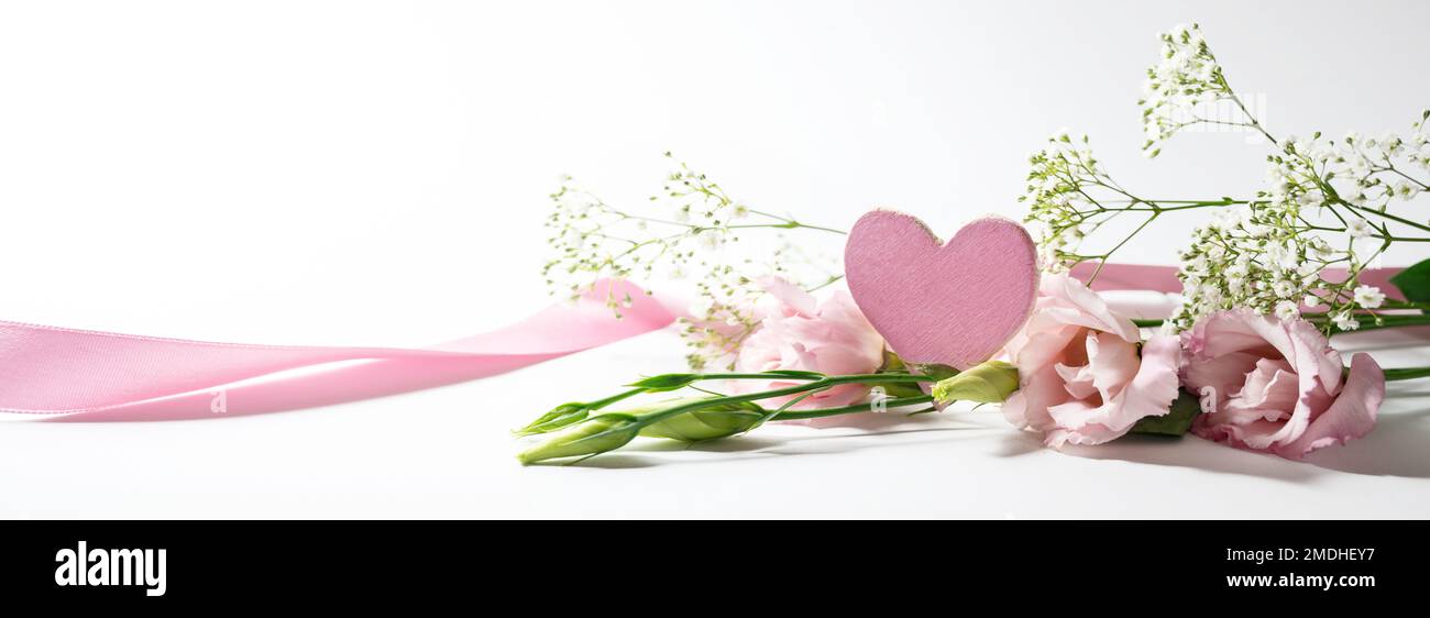 Pink wooden heart shape, long ribbon and flowers in panoramic banner format on a white gray background, romantic love symbol for holidays, copy space, Stock Photo