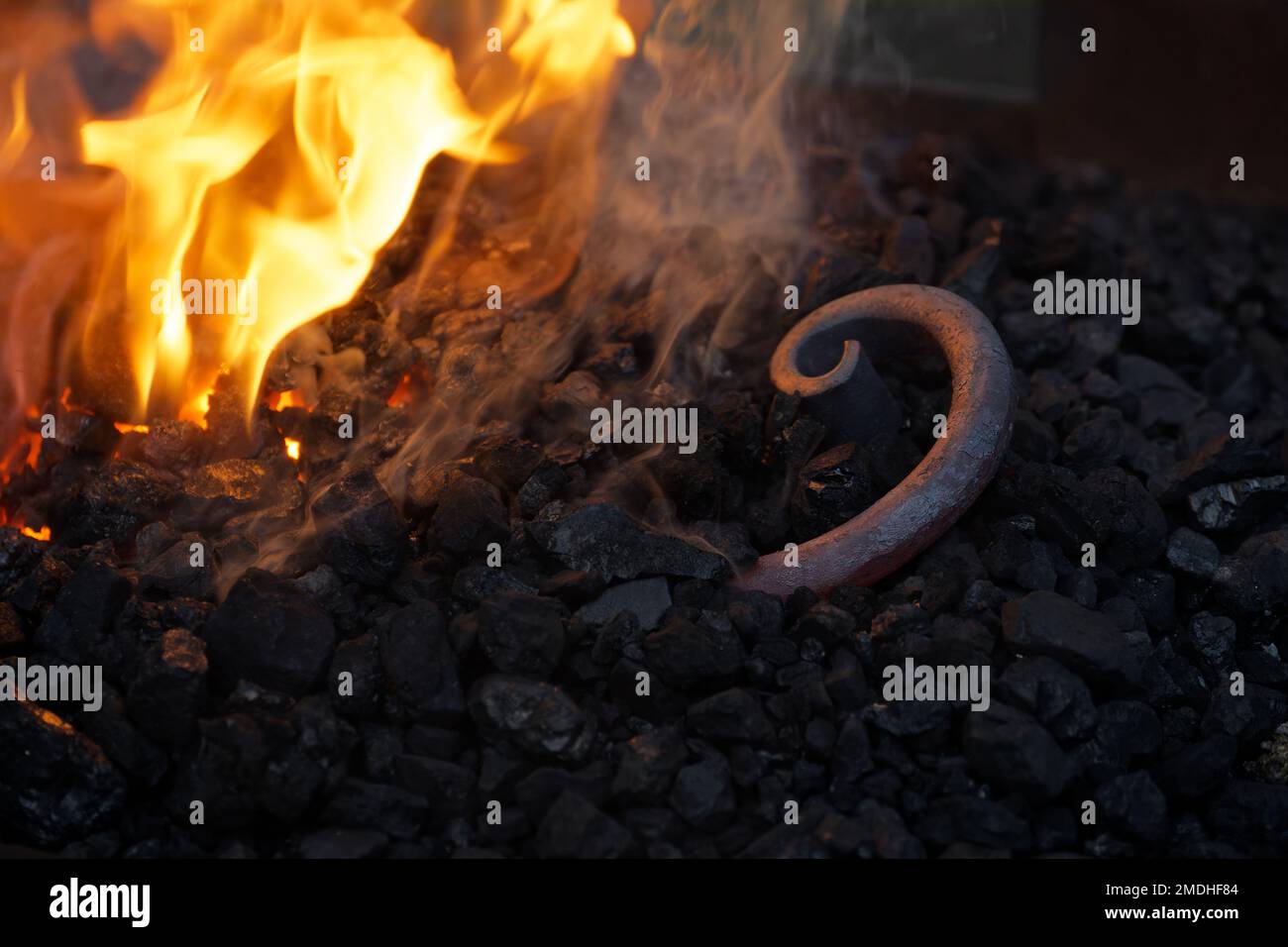 Spiral of an iron rod lying in the coal from the forge fire og the blacksmith to be heated again, copy space in the dark background, selected focus, n Stock Photo