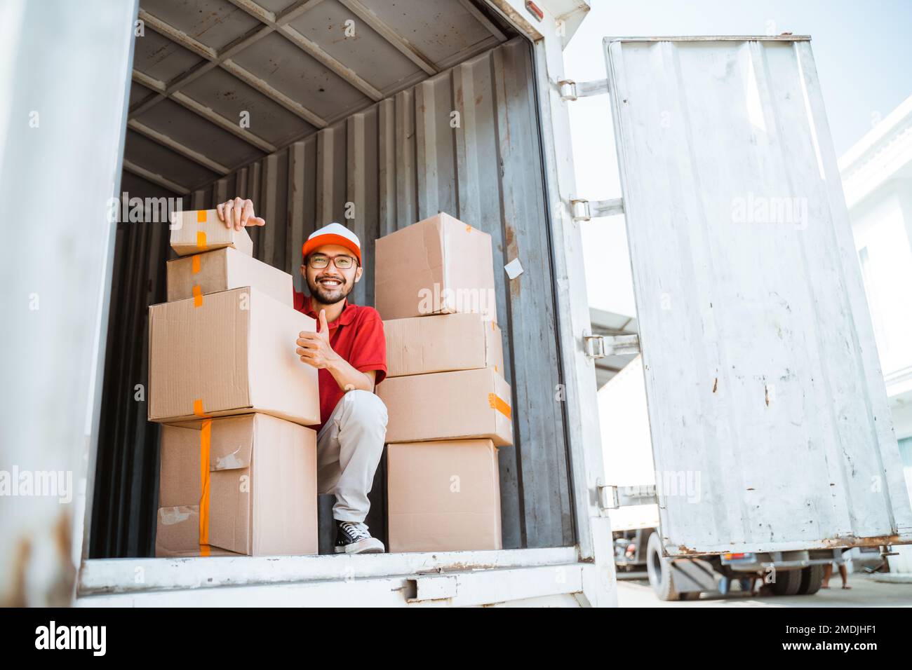 Smiling male employee with thumbs up while working unloading boxes Stock Photo