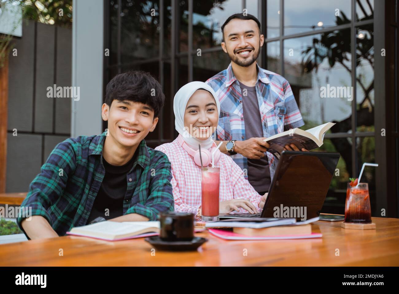 three smiling Asian students looking at camera while studying together ...