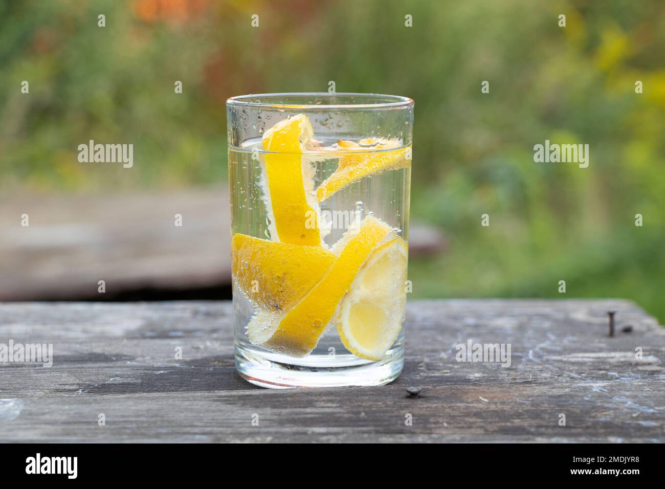 carbonated water with pieces of lemon in a glass on a wooden table outside, lemon juice in a glass, drink, lemonade Stock Photo