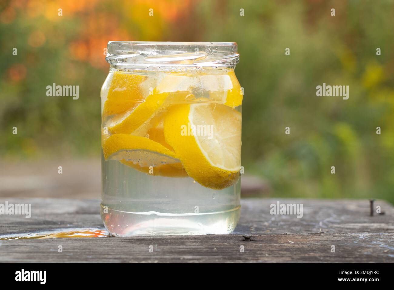 carbonated water with pieces of lemon in a glass on a wooden table outside, lemon juice in a glass, drink, lemonade Stock Photo