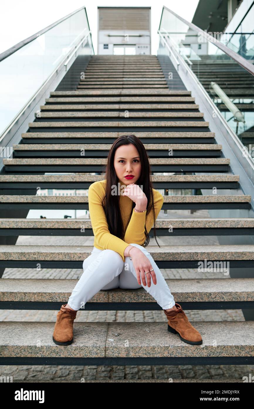 Woman looking at the camera while sitting on stairs outdoors. Stock Photo