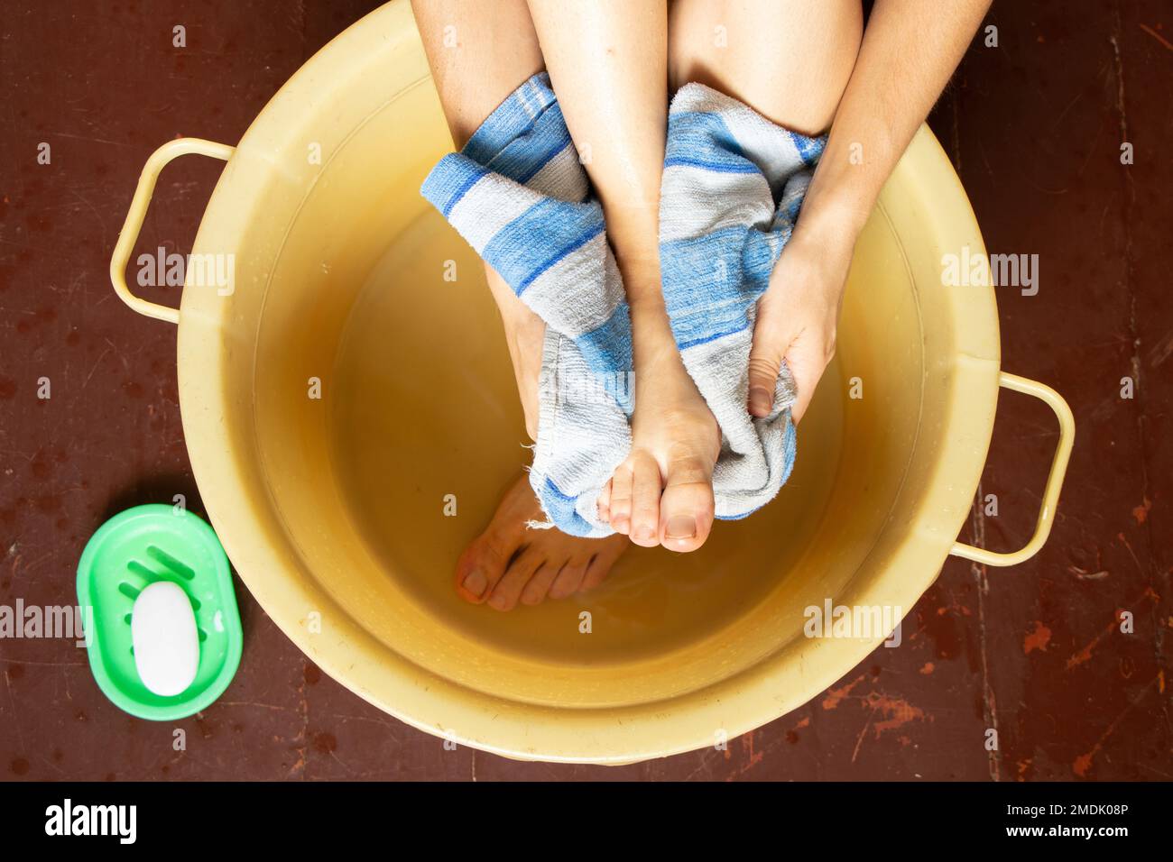 girl washes her feet in a bowl of water on the wooden floor at home, foot care, wash feet at
