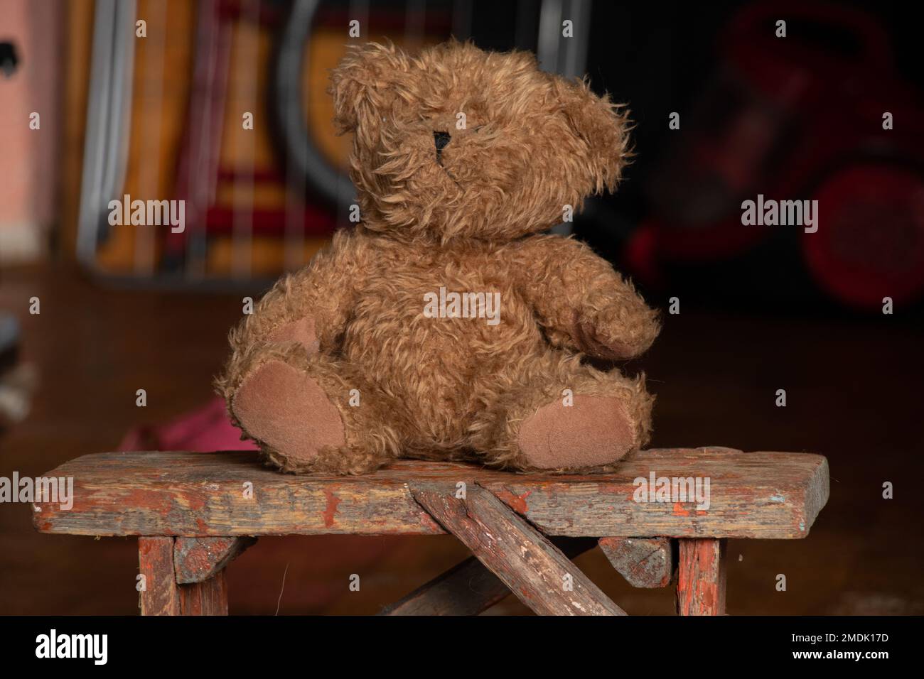 old dirty teddy bear sits on a bench in a dark room at home, abandoned and lonely, poverty Stock Photo