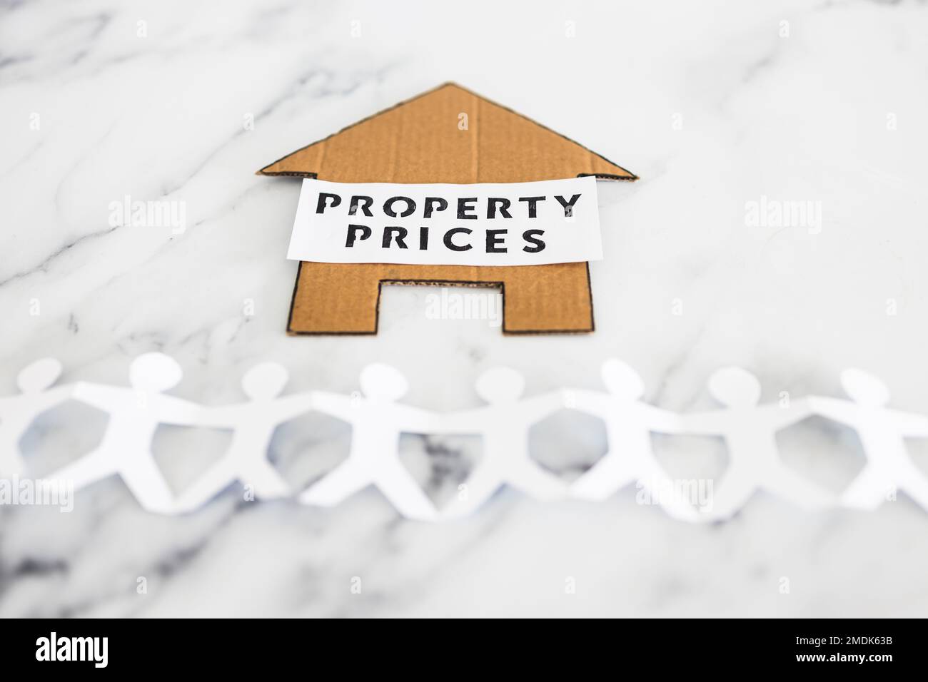 real estate affordability conceptual image, property prices text on cardboard house with paper people chain underneath symbol of potential clients Stock Photo