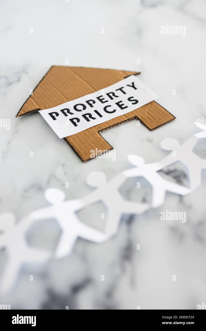 real estate affordability conceptual image, property prices text on cardboard house with paper people chain underneath symbol of potential clients Stock Photo