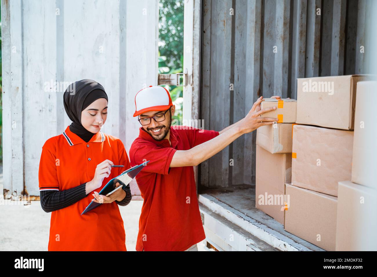 two young workers in red uniforms manage boxed products Stock Photo