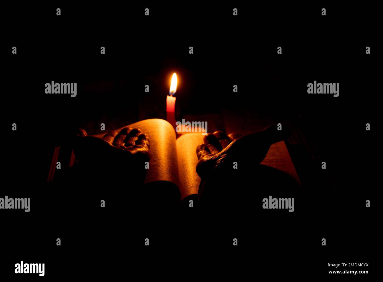 bible lies a candle flame of a candle in the dark, pray a bible, hands on a book and a candle flame at night, religion Stock Photo