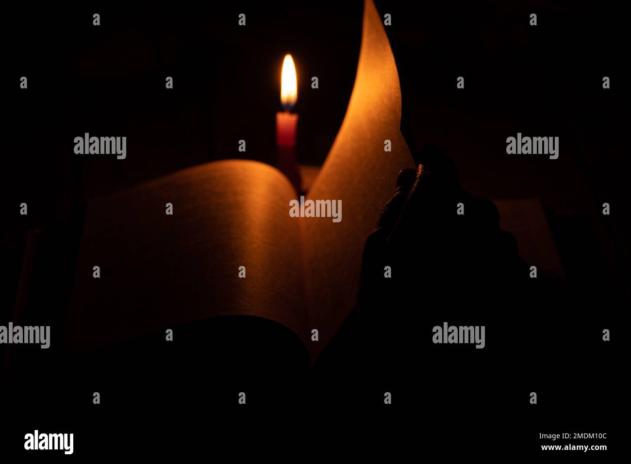 bible lies a candle flame of a candle in the dark, pray a bible, hands on a book and a candle flame at night, religion Stock Photo