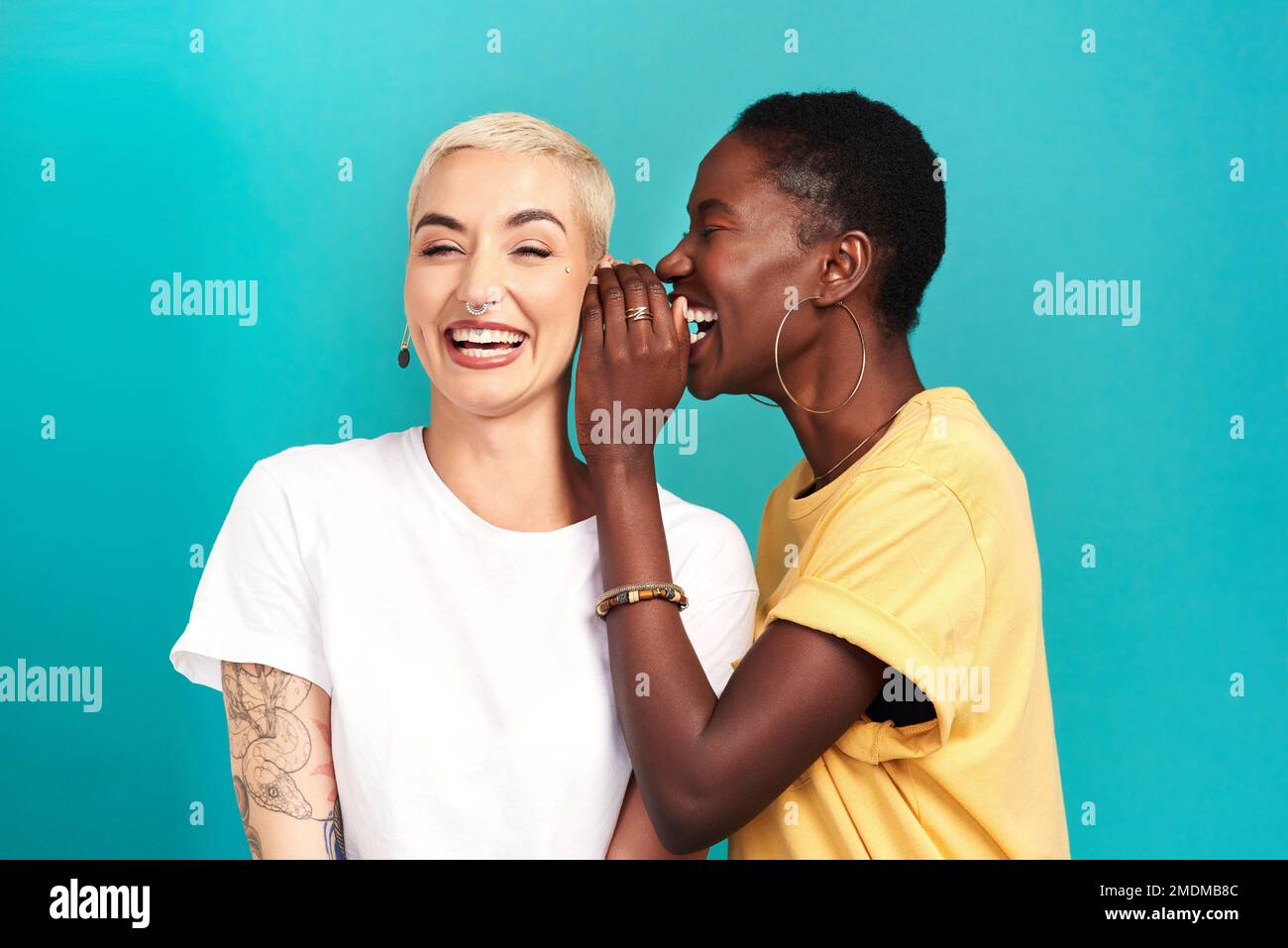 Youre not gonna believe this but.Studio shot of a young woman whispering in her friends ear against a turquoise background. Stock Photo
