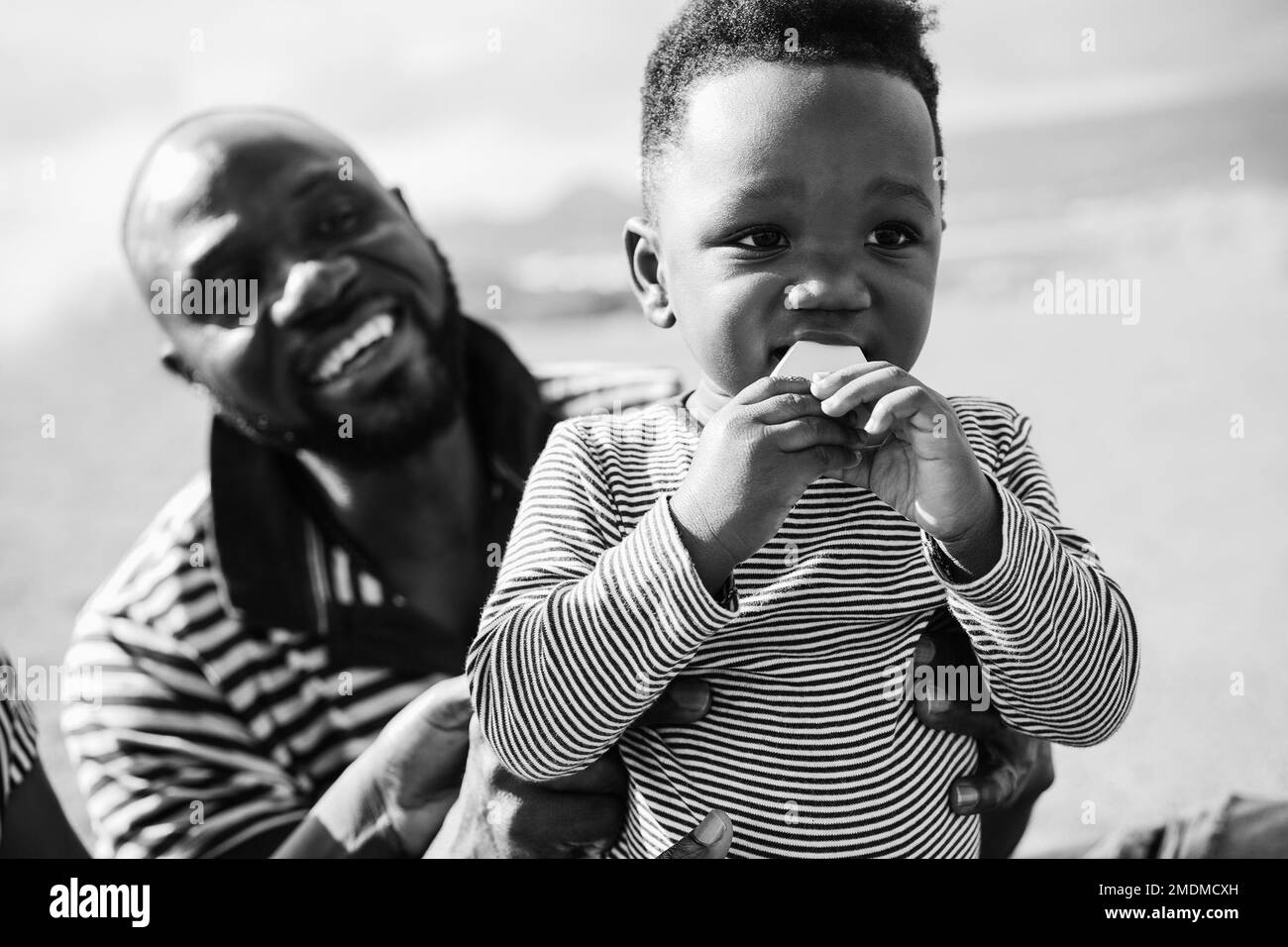 African father and son having fun on the beach during vacations - Focus on toddler face - Black and white editing Stock Photo