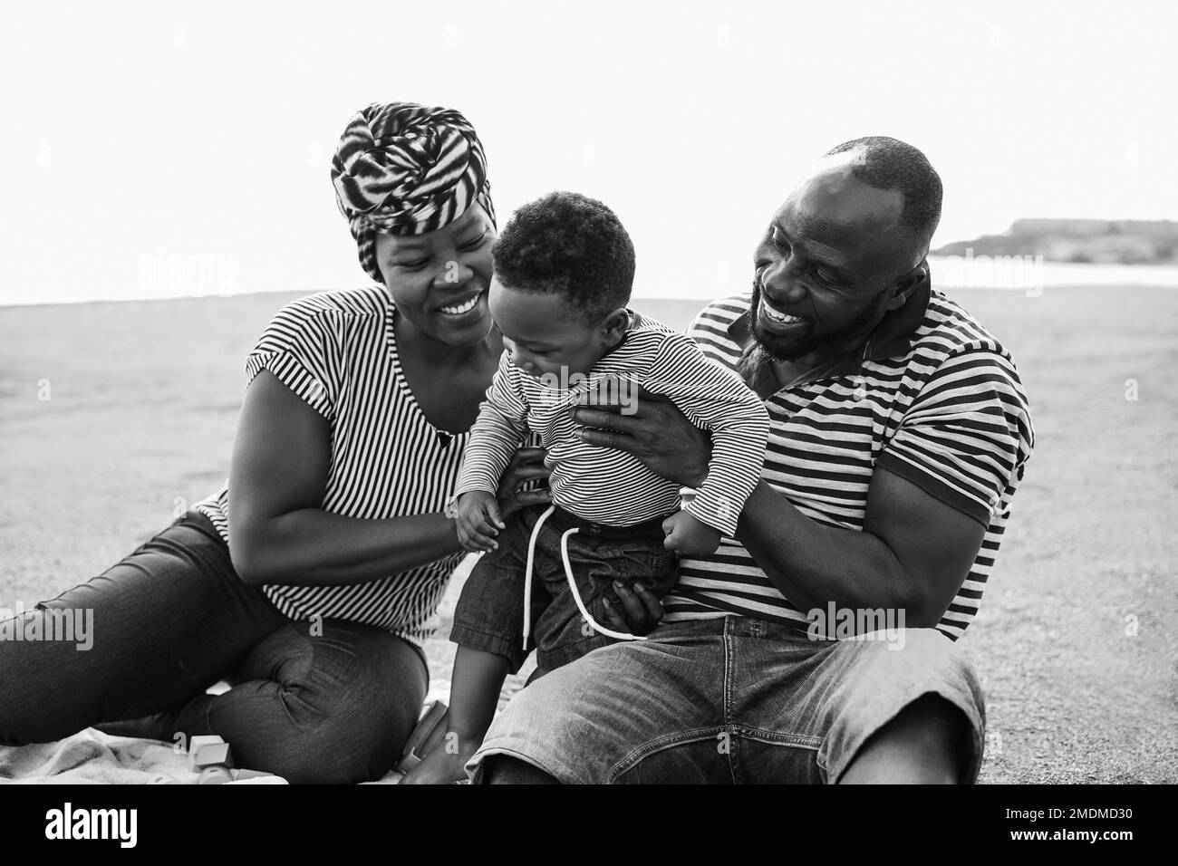 African family having fun on the beach in summer vacation - Main focus on father hand - Black and white editing Stock Photo