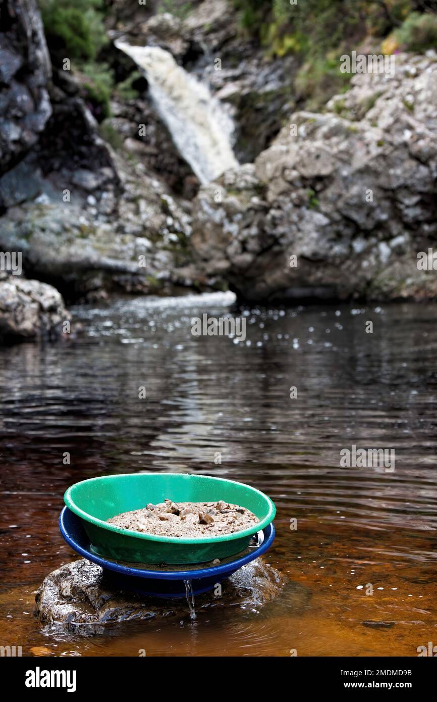 A gold pan filled with river gravals sitting on a rock in the Kildonan Burn in the Highlands of Scotland Stock Photo