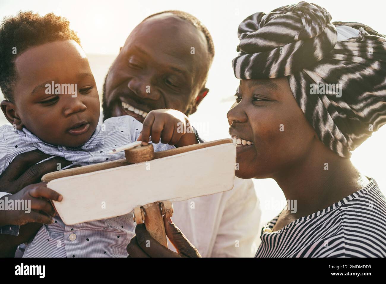 African parents and little son having fun with wood airplane on the beach - Focus on kid face Stock Photo