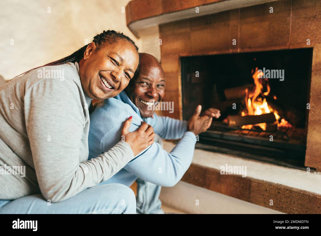 Senior african american couple warming up next to fireplace inside mountain chalet - Winter lifstyle and love concept - Main focus on woman face Stock Photo