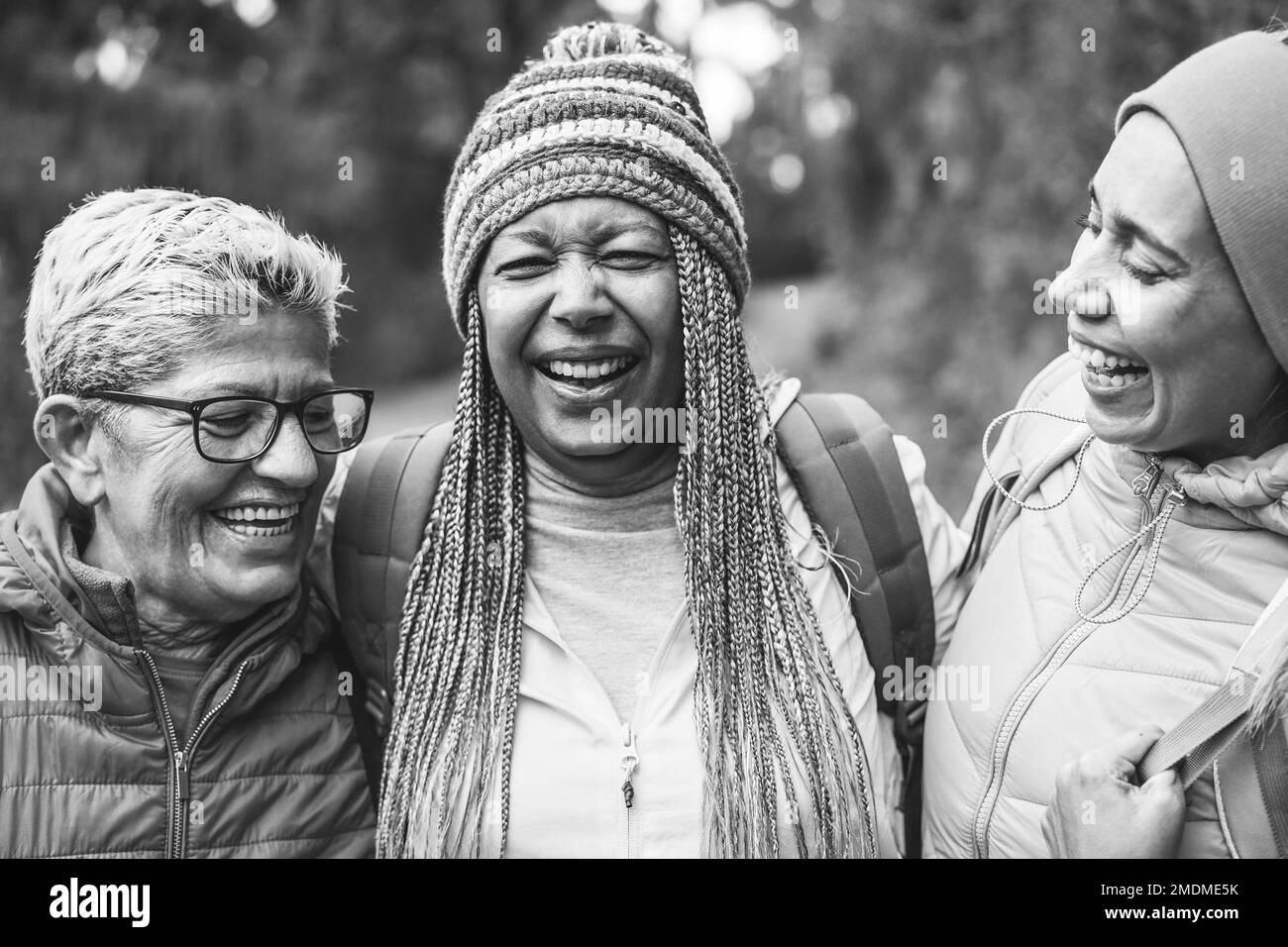 Multiracial senior female friends having fun during trekking day in mountain forest - Focus on african female face - Black and white editing Stock Photo