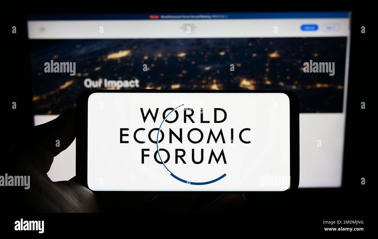 Person holding mobile phone with logo of organisation World Economic Forum (WEF) on screen in front of web page. Focus on phone display. Stock Photo