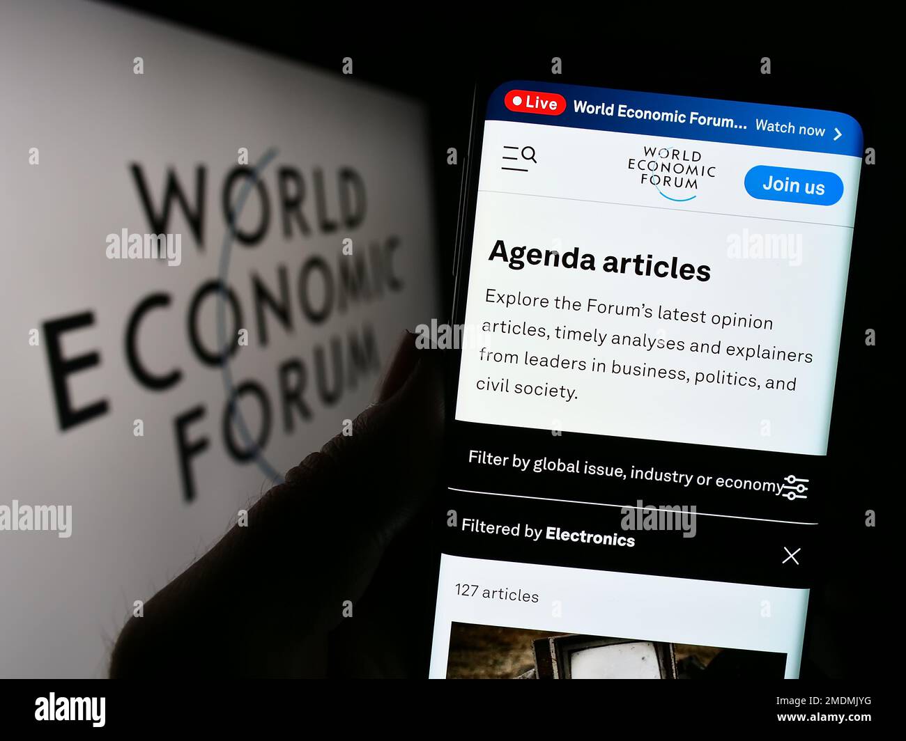 Person holding cellphone with webpage of organisation World Economic Forum (WEF) on screen in front of logo. Focus on center of phone display. Stock Photo