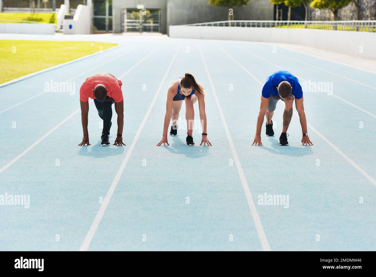 Ready for a race. Full length shot of three young athletes in the set position out on the running track. Stock Photo