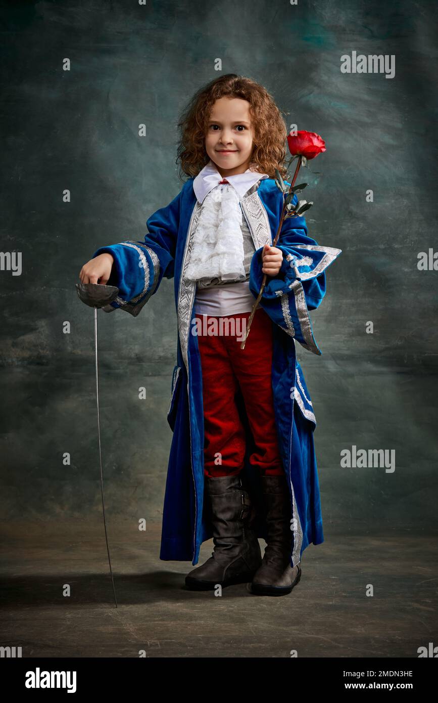 Cinematic portair of beautiful little girl dressed up as medieval knight, little prince over dark vintage style background, Fashion, beauty, emotions Stock Photo