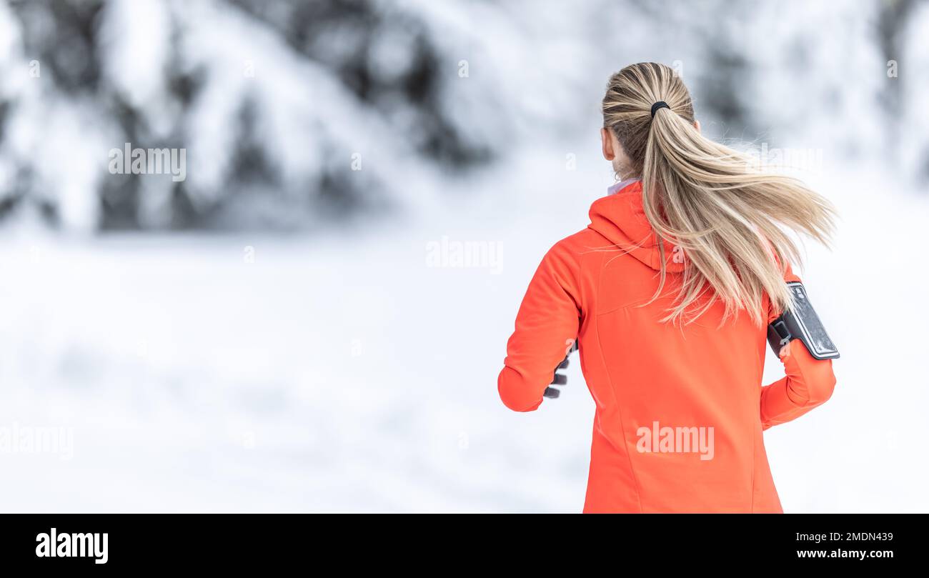 Running in winter, rear view of a female runner on a snowy path in a