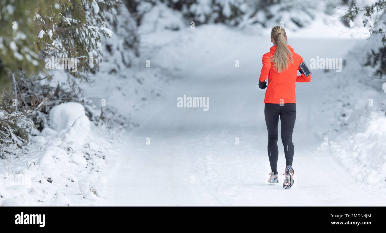 Running in winter, rear view of a female runner on a snowy path in a park or forest. Stock Photo