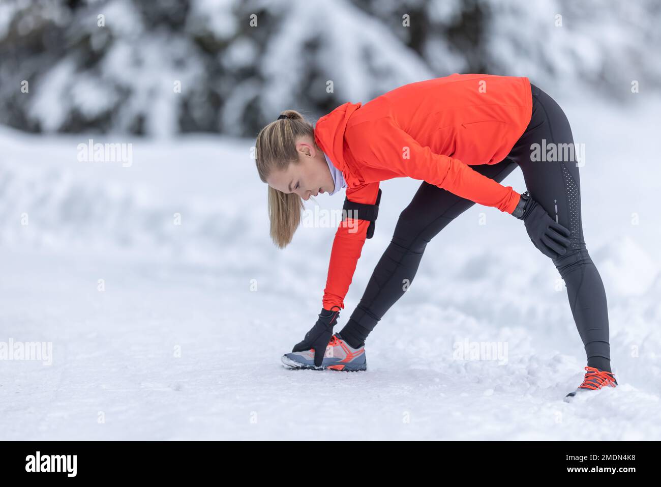 Athletic female runner doing stretching exercise, preparing for workout in the snowy winter park. Stock Photo