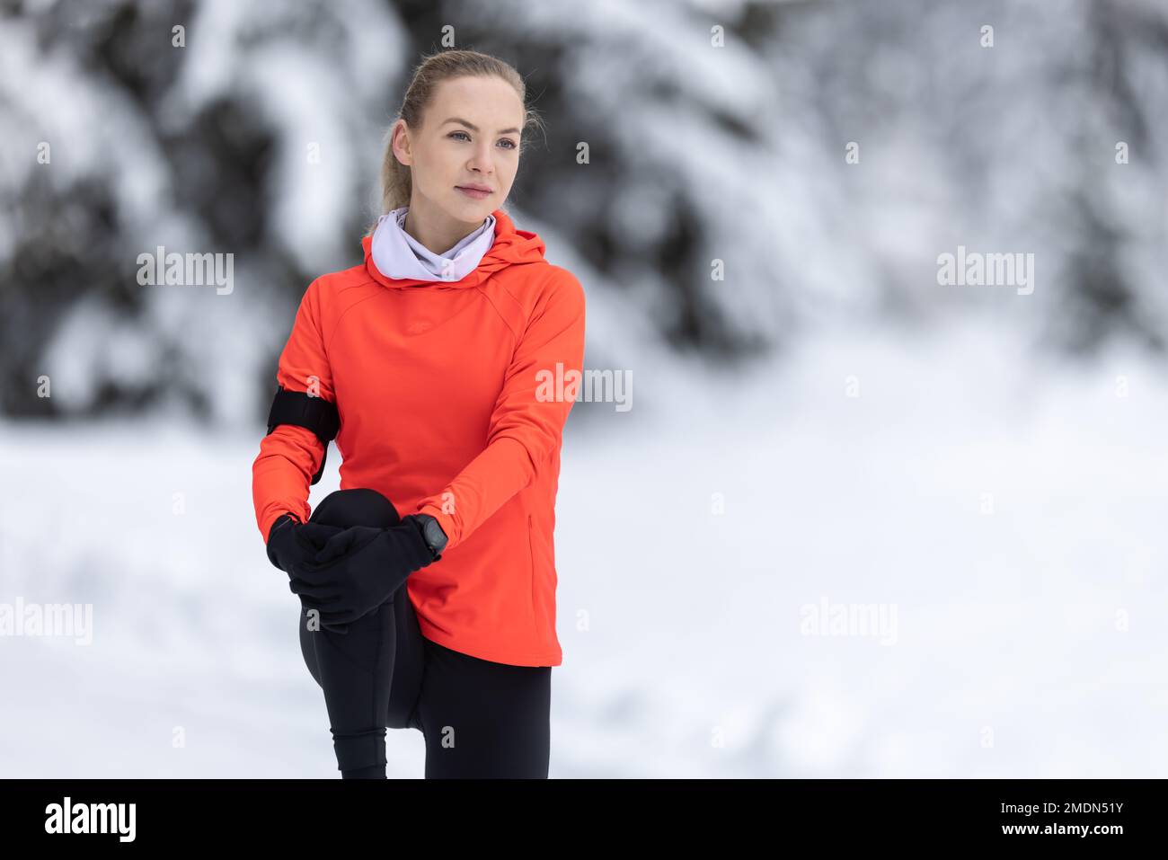 Athletic female runner doing stretching exercise, preparing for workout in the snowy winter park. Stock Photo