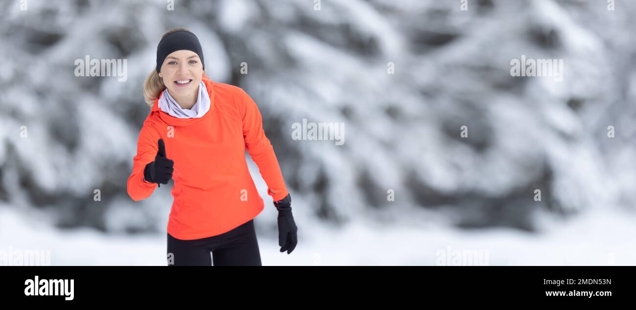 Fit woman and thumbs up for running in nature or healthy workout run with smile in the winter outdoors. A motivational gesture for sports and movement Stock Photo