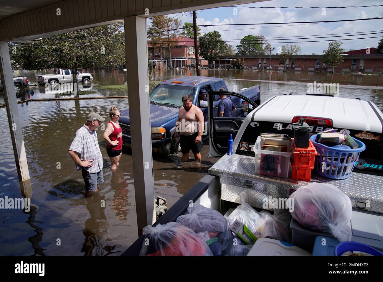 People stand in floodwaters while salvaging items from their flood