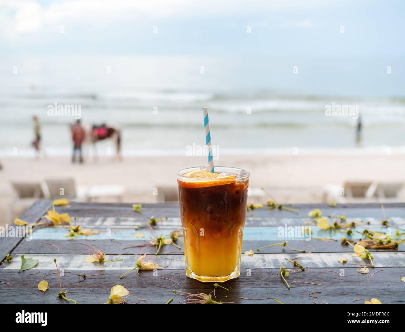 A glass of fresh iced orange americano decorated with sliced orange served on wooden table on the beach background, seascape view. Cold black coffee Stock Photo