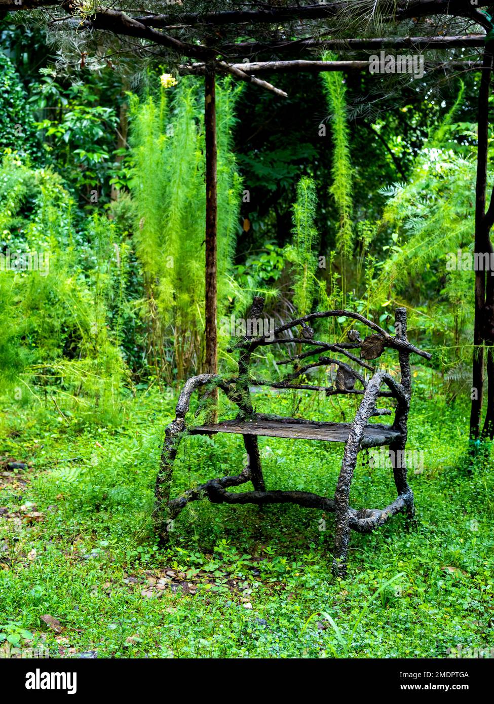 Empty old lonely vintage iron bench seat, chair at the desolate yard on the green forest background, vertical style. Stock Photo
