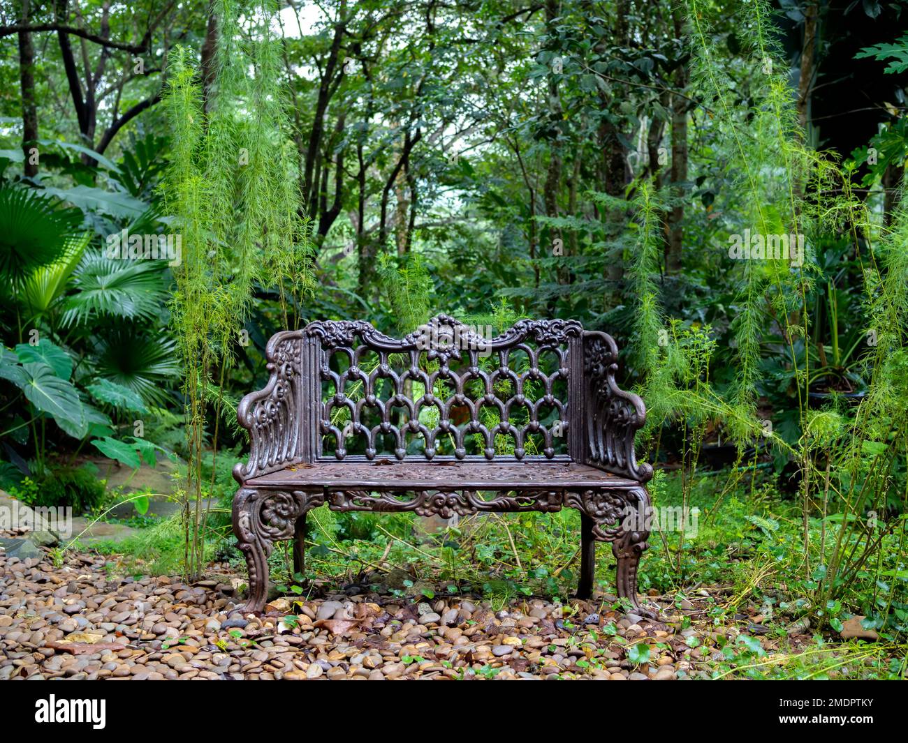 Empty old lonely vintage iron bench seat, chair at the desolate yard on the green forest background. Stock Photo