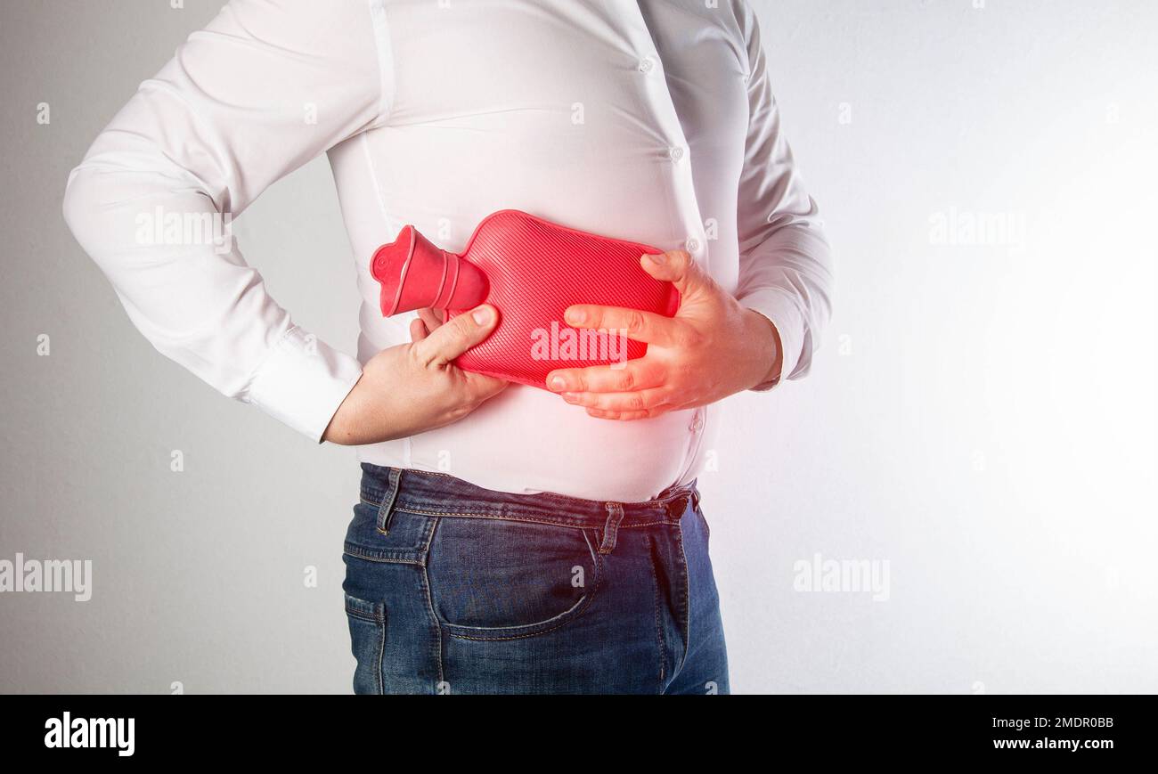 The man holds a heating pad with hot water on the abdominal wall on the right. Relieve muscle spasms and pain near diseased internal organs. Thermothe Stock Photo