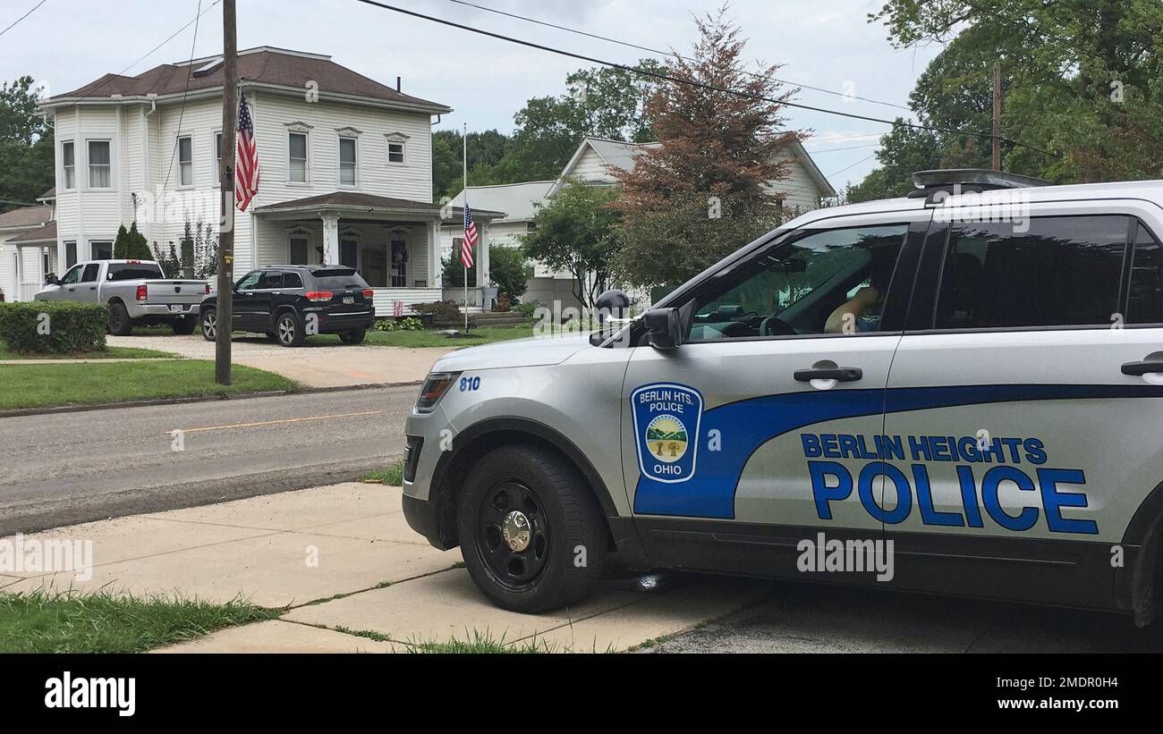 A Berlin Heights police officer sits across the road from the home of