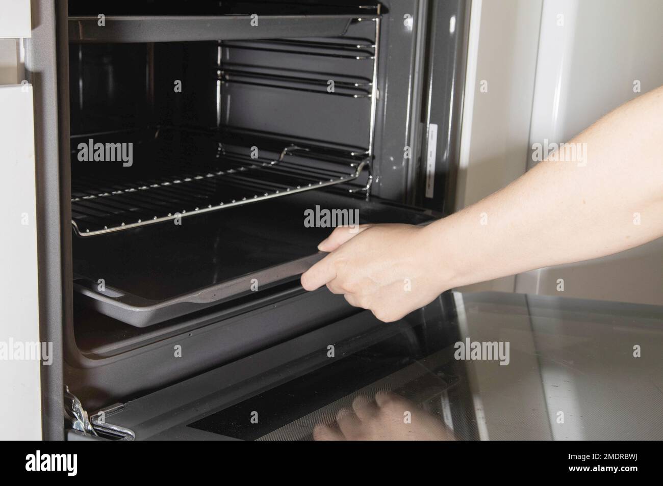 The girl takes out a metal baking sheet from the stove oven to clean it
