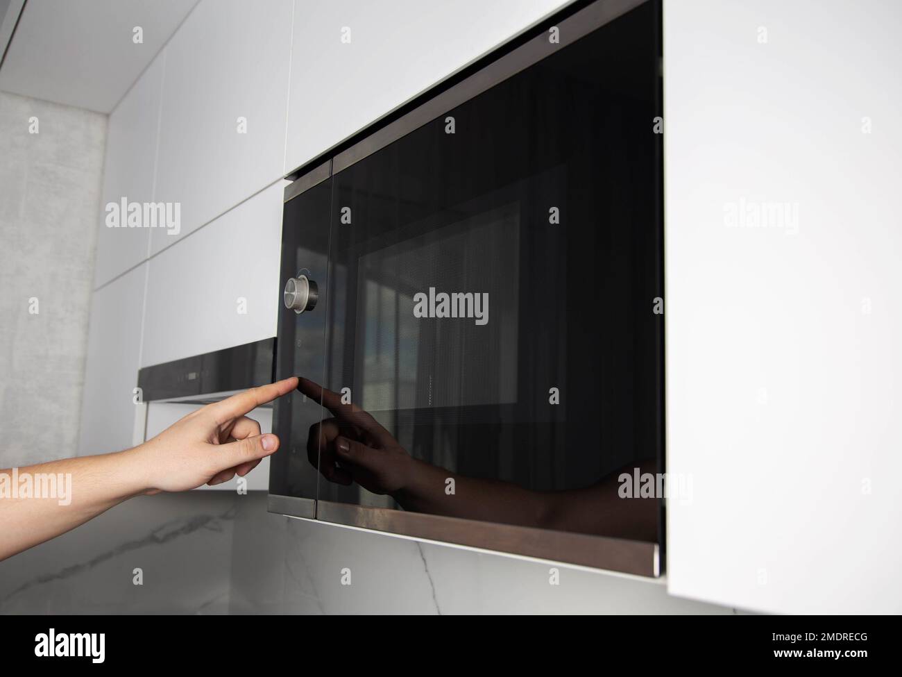A man presses his finger on the touch panel of a microwave oven to turn