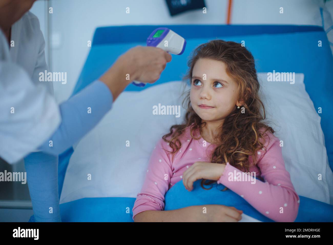 Nurse measuring body temperature to little girl lying in the hospital. Stock Photo