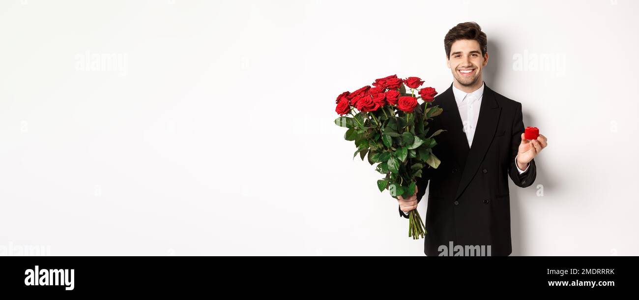 Image of handsome man in black suit, holding bouquet of red roses and a ...