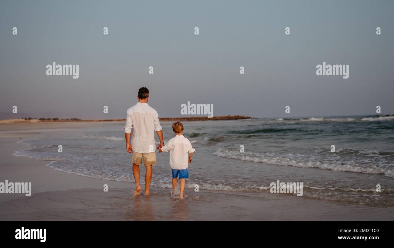Rear view of father and his son walking on the beach, enjoying summer vacation. Stock Photo