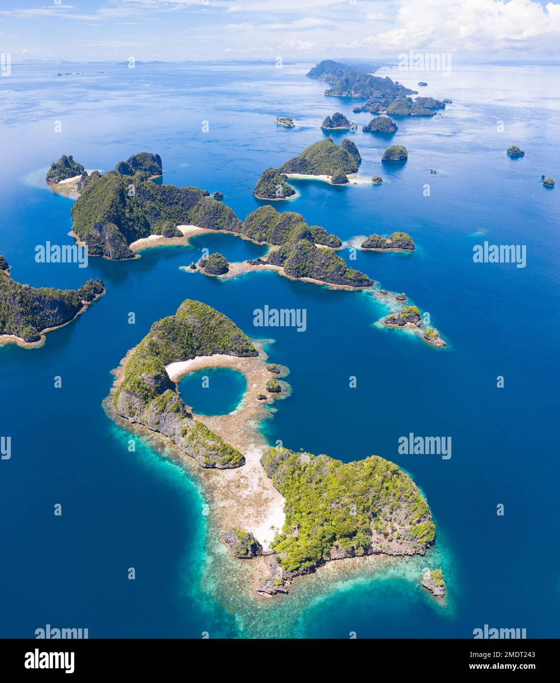Rock islands, composed of limestone, rise from the tropical seascape in Raja Ampat, Indonesia. These islands are ancient, uplifted coral reefs. Stock Photo