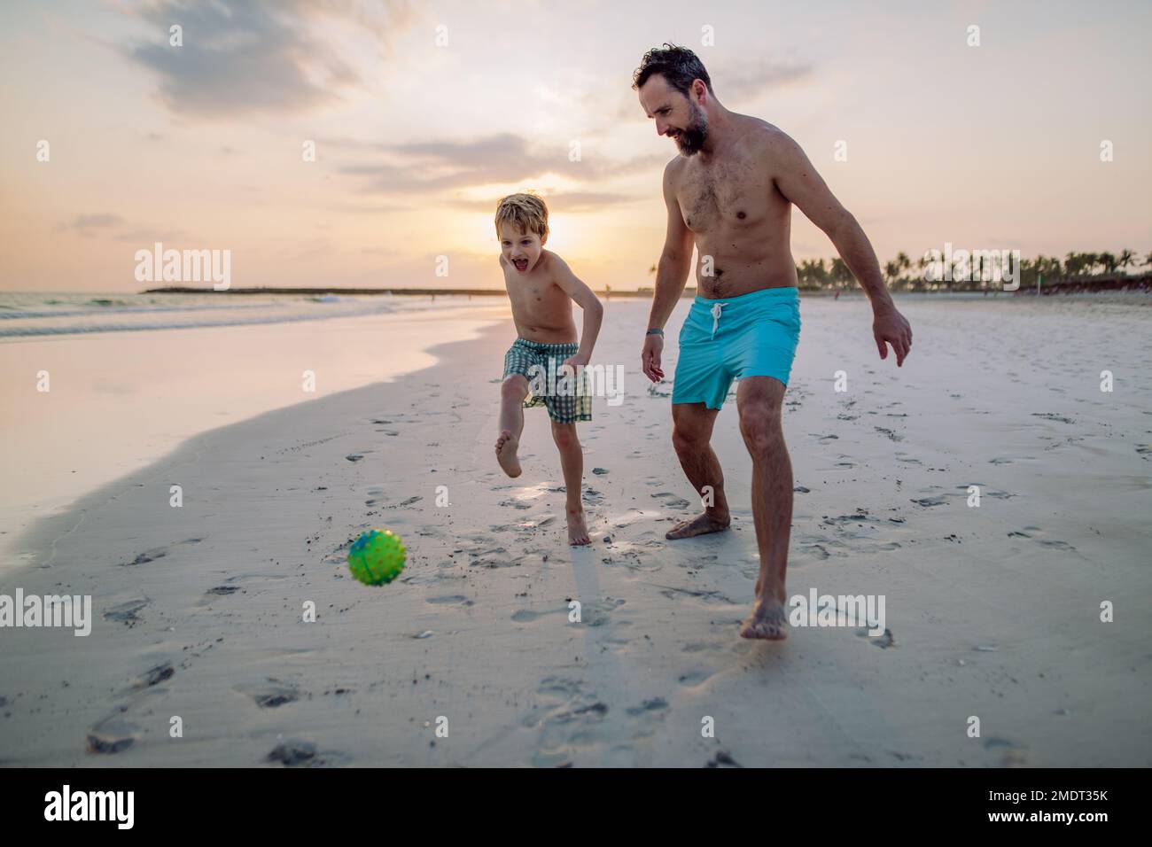 Father with his son plaing football on the beach. Stock Photo