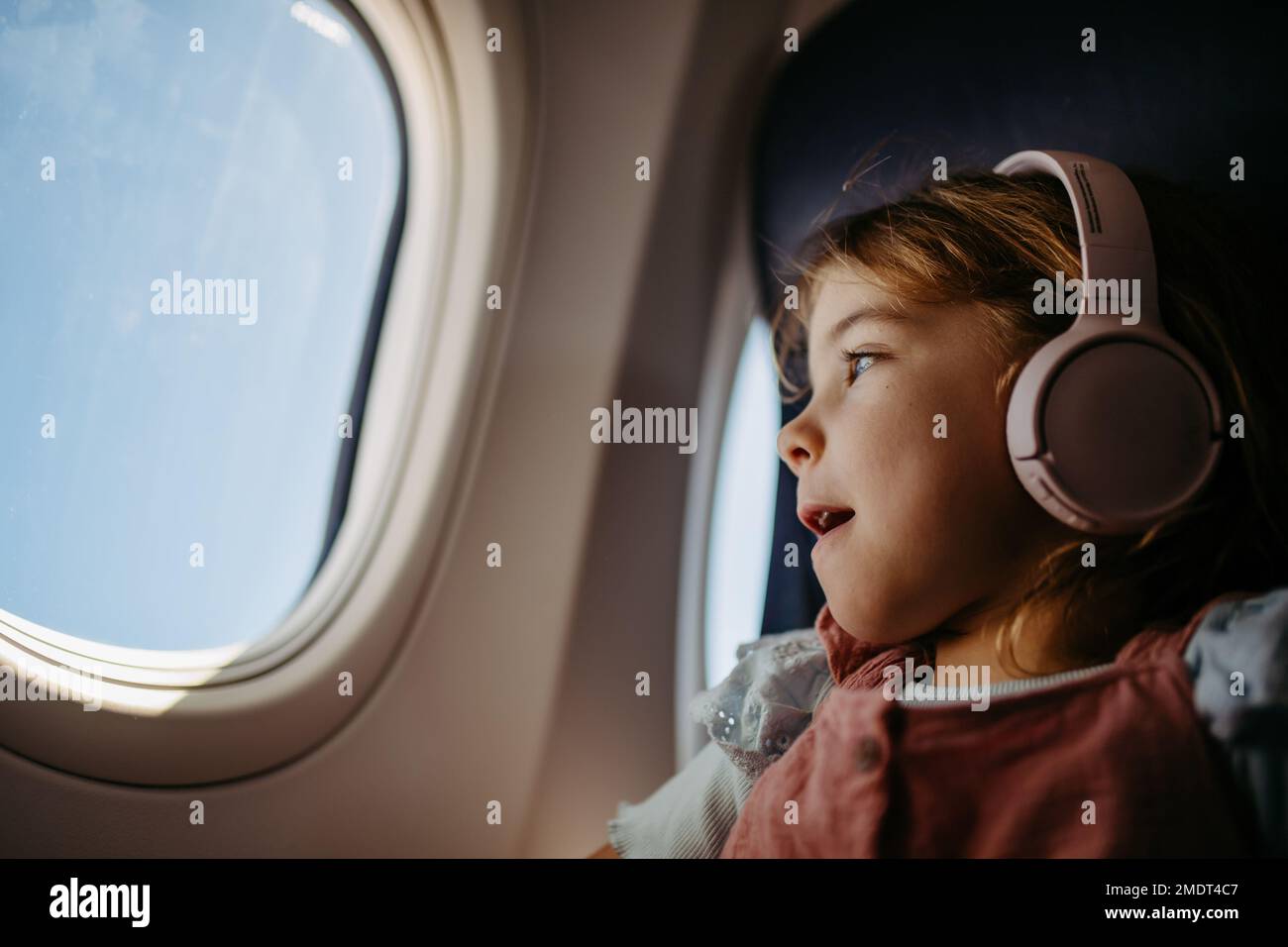 Little girl in airplane looking out of the window. Stock Photo