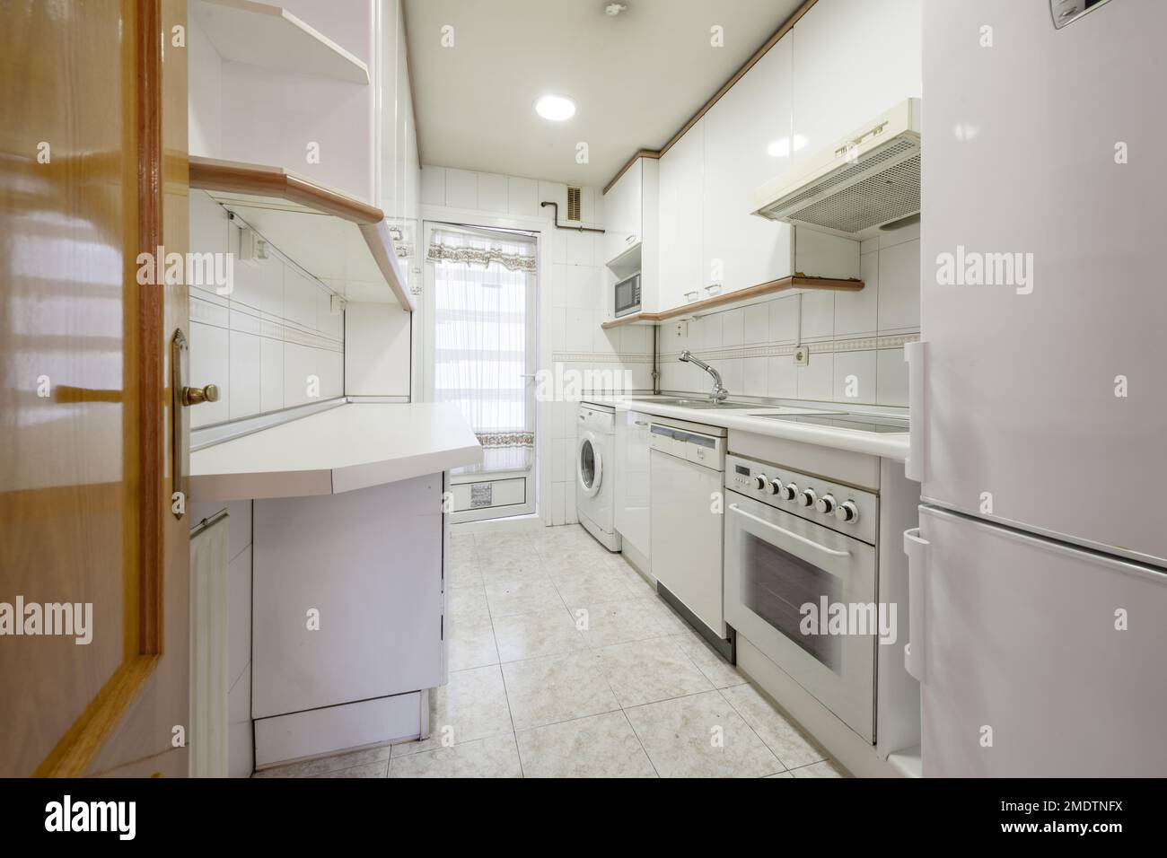 Narrow kitchen with white with countertop of the same color and builtin appliances of