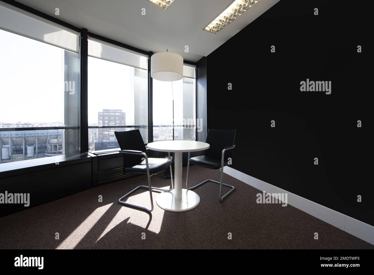 Office with a small white round table next to a large window with a