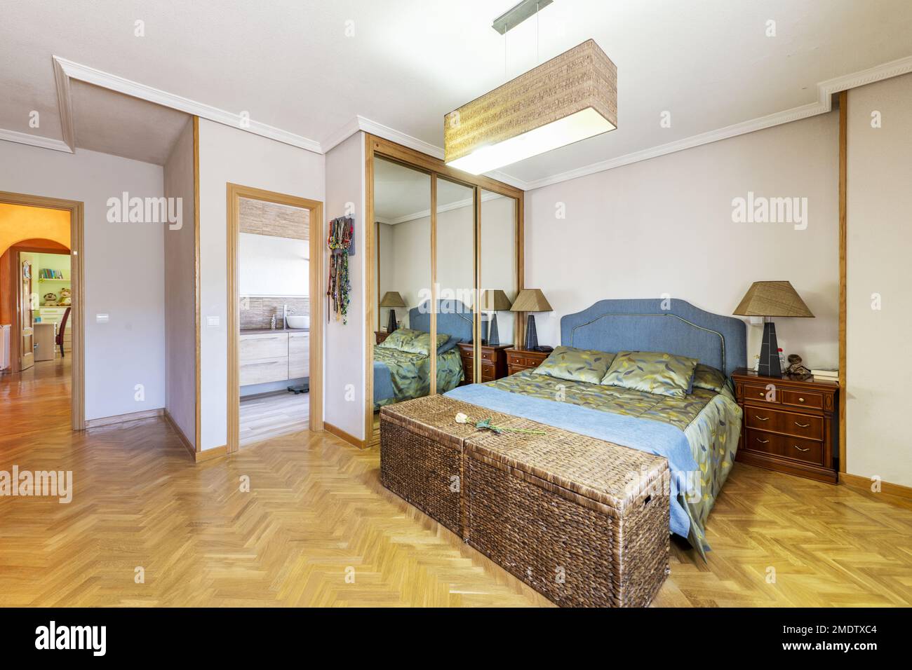 Bedroom with built-in three-section wardrobe, en-suite toilet and wicker trunks at the foot of the bed Stock Photo